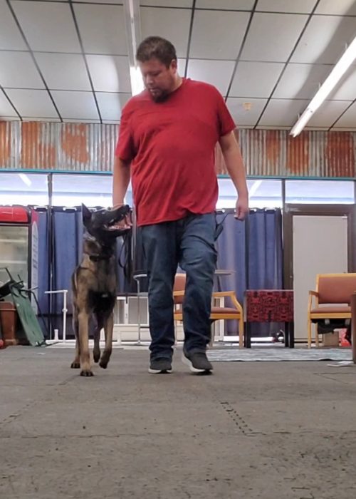 A man walking his dog on a leash through a dimly lit warehouse